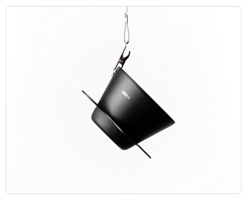 The black Orea brewer suspended at an angle by a metal clip and wire against a clean white background.