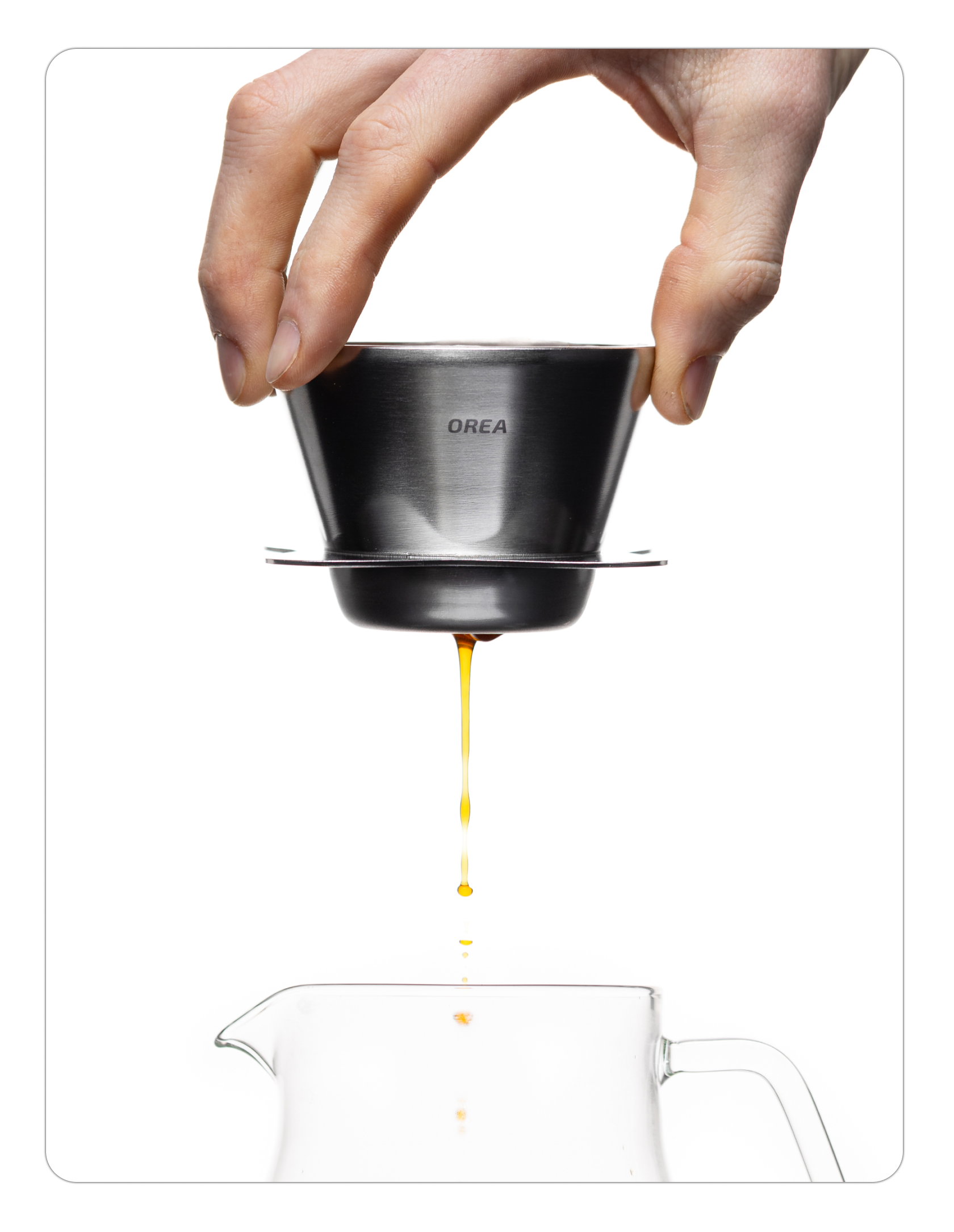 A person holding the silver stainless steel Orea O1 brewer over a carafe while coffee drips from the bottom. The shot highlights the raw metallic finish and the active filtration process.