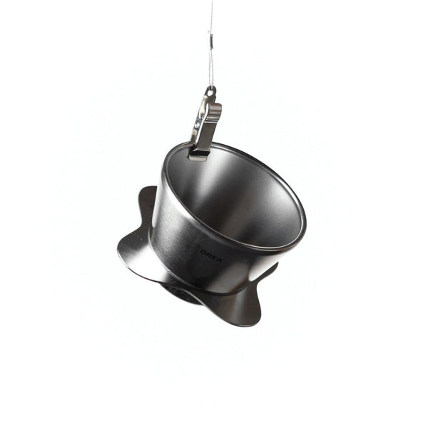 A front-facing view of the Orea 01 brewer hanging vertically from a metal clip, showcasing its minimalist conical shape.