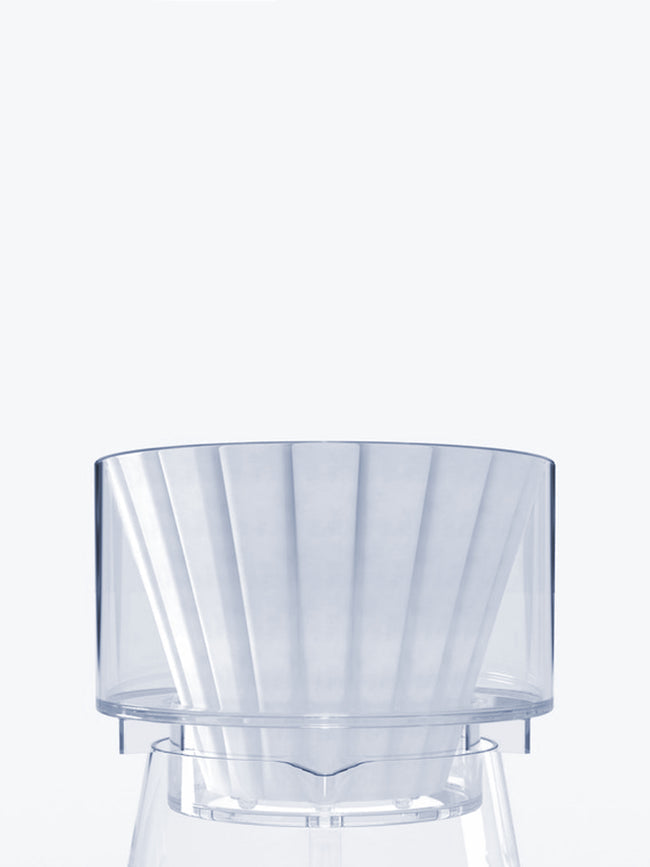 A close-up shot of the transparent Bathtub Simplify Brewer with a paper filter inside, resting securely on the rim of a glass decanter.
