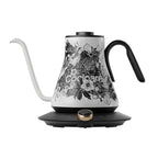 Blossom Cocinare Gooseneck Kettle with a digital display and a pot of coffee beans on top, alongside a Cocinare Balance Precision Coffee Scale with a digital display showing weight, on a blue background with scattered coffee beans and a coffee bag.