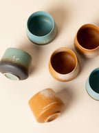 An overhead flat lay of Somewhere Coffee Co.'s handmade ceramic cups, featuring a textured matte finish and beautiful reactive glaze in teal and warm amber tones, crafted in collaboration with Not Just a Cup.