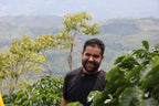 A proud Colombian coffee grower standing among the lush green coffee plants with the misty mountains of Pitalito, Huila in the background at Laboyani Farm, the source of Somewhere Coffee's Washed Gesha.