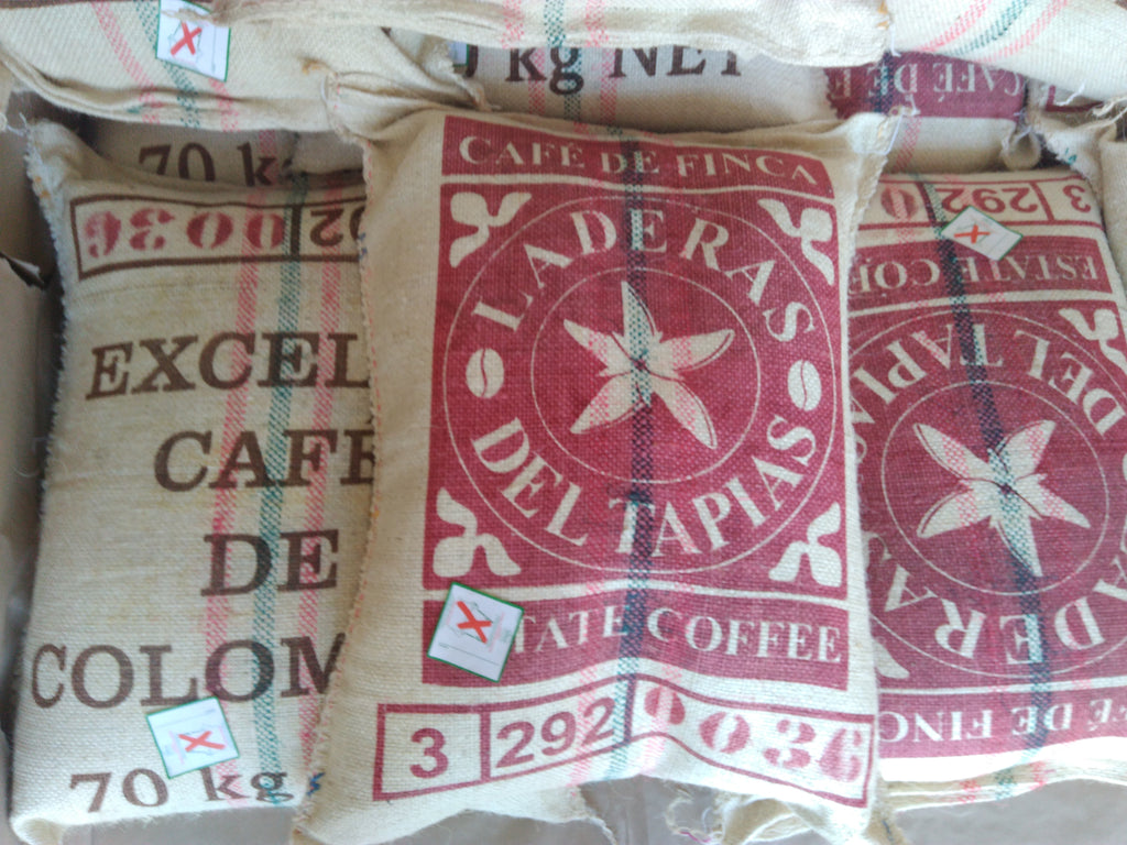Close-up of stacked, traditional jute export bags branded with "LADERAS DEL TAPIAS" and "CAFE DE FINCA" at the farm in Neira, Caldas, Colombia. These 70kg bags hold the natural, patio-dried Catiope coffee ready for export to Somewhere Coffee.