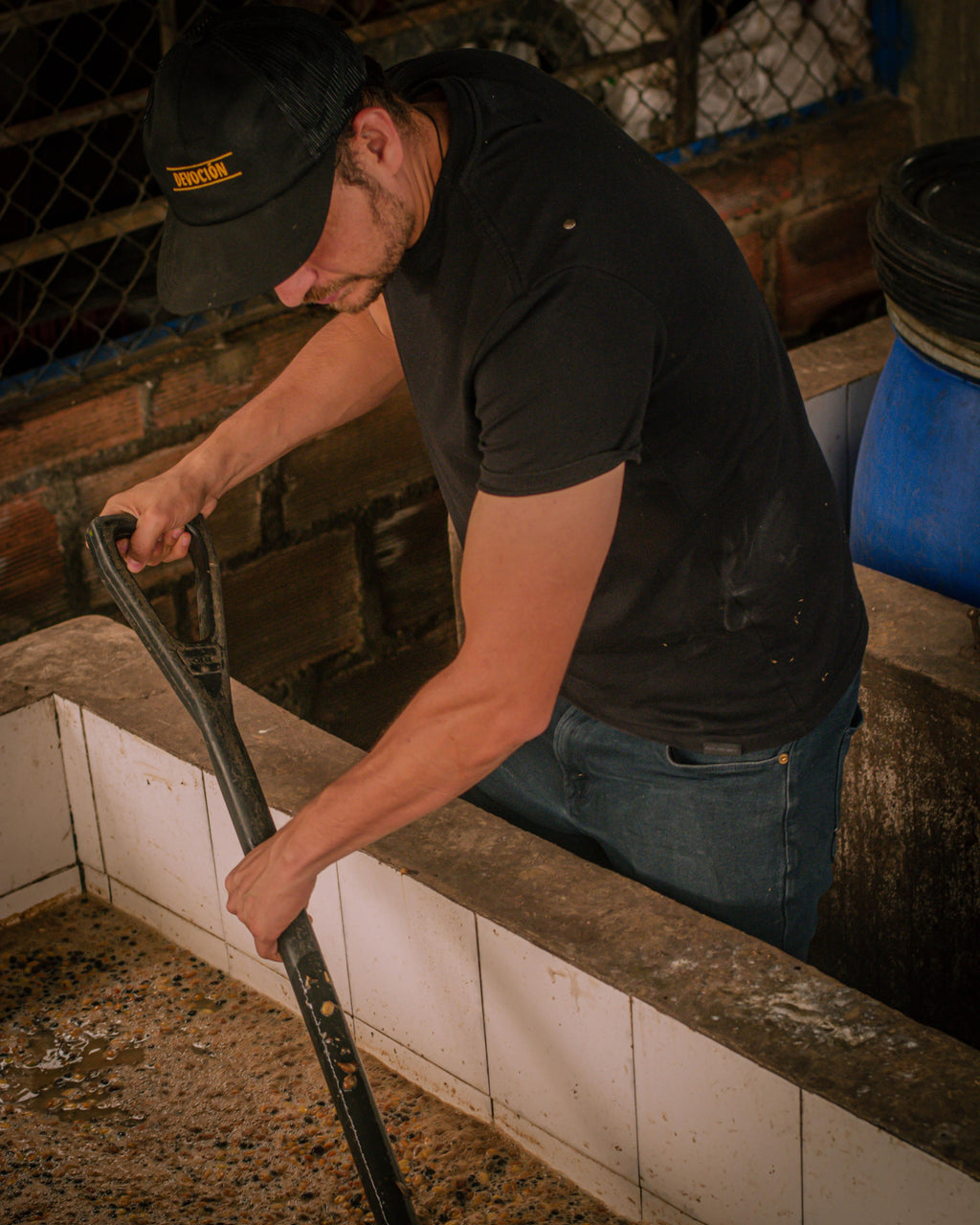Producer Marlon Rojas intensely focused as he uses a long stirring tool to agitate the coffee beans inside a white-tiled fermentation tank at La Reserva Farm in Pitalito, Huila, managing the precise 72-hour submerged oxidation process for Somewhere Coffee.