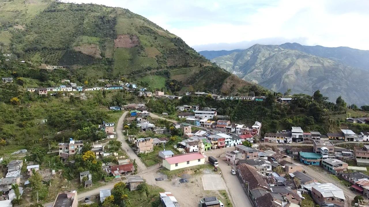 An aerial drone shot of a colorful, rural mountain town nestled in the steep, lush green hills of Nariño, Colombia. The winding roads and scattered homes sit at over 2000 masl, serving as the home for the indigenous smallholder communities who grow the washed Castillo beans for Somewhere Coffee's Nariño Reserve.