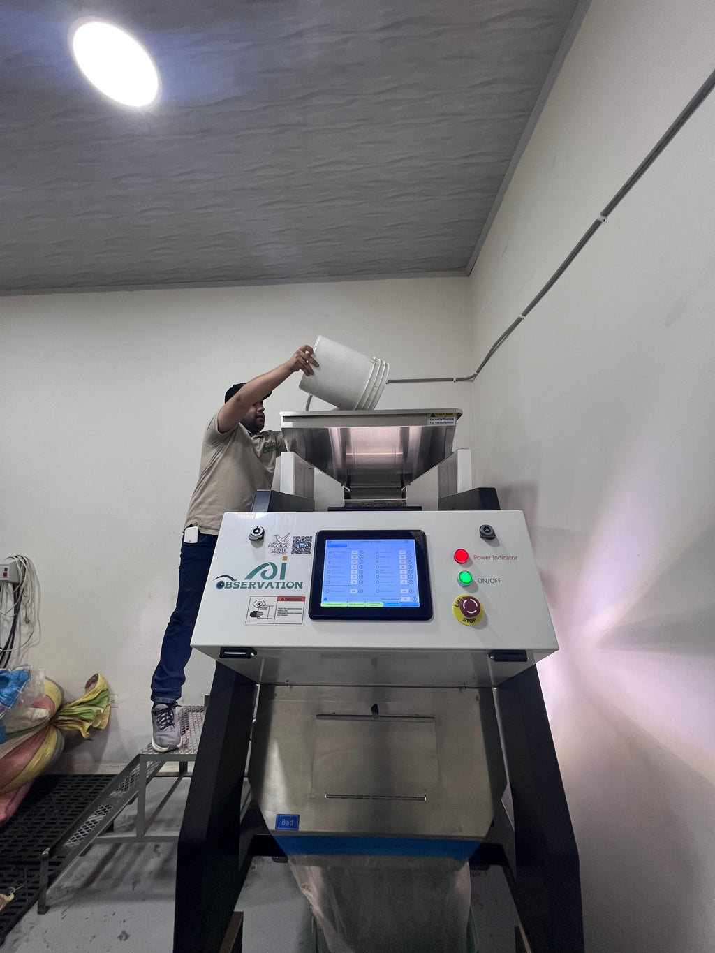 A worker pouring beans into a high-tech optical color sorter to remove defects, ensuring only the best Washed Gesha beans from Laboyani Farm make it into Somewhere Coffee's roast.