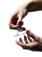 An action shot showing two hands carefully snapping a black OREA Regulator (the #4 medium flow version) into the bottom of a clear OREA O1/O2 brewer, demonstrating how easy the modular system is to change.