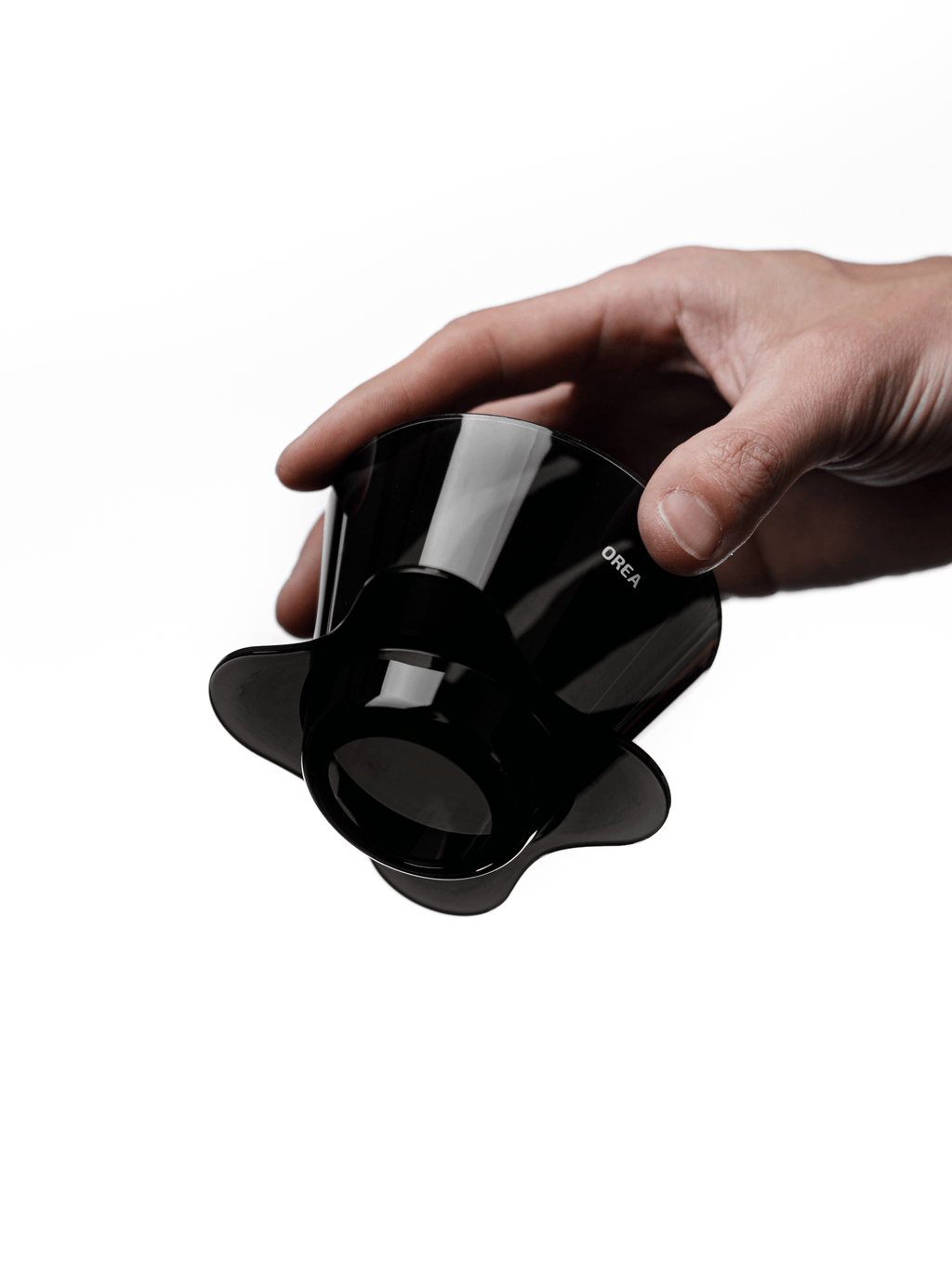A hand holding the compact OREA O2 brewer angled upwards, clearly displaying the open bottom and wide base designed to direct water centrally through the coffee bed for a balanced brew.