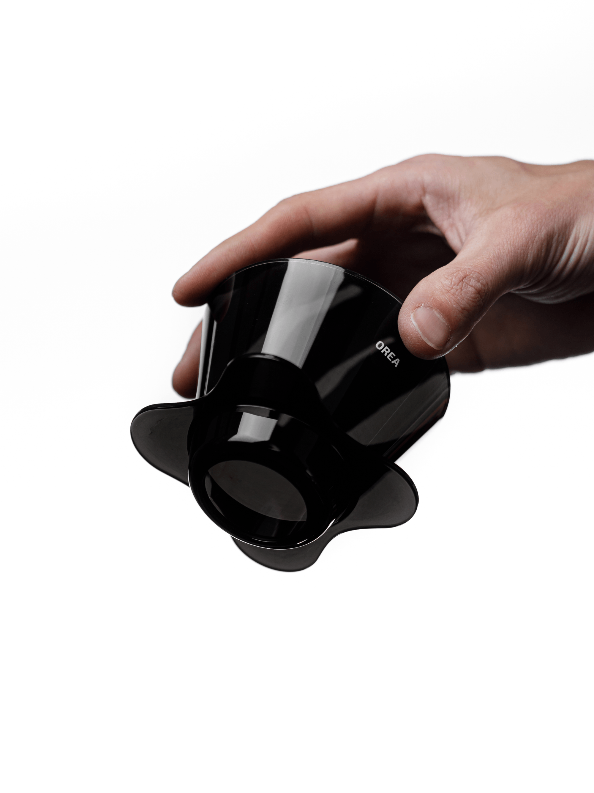A hand holding the compact OREA O2 brewer angled upwards, clearly displaying the open bottom and wide base designed to direct water centrally through the coffee bed for a balanced brew.