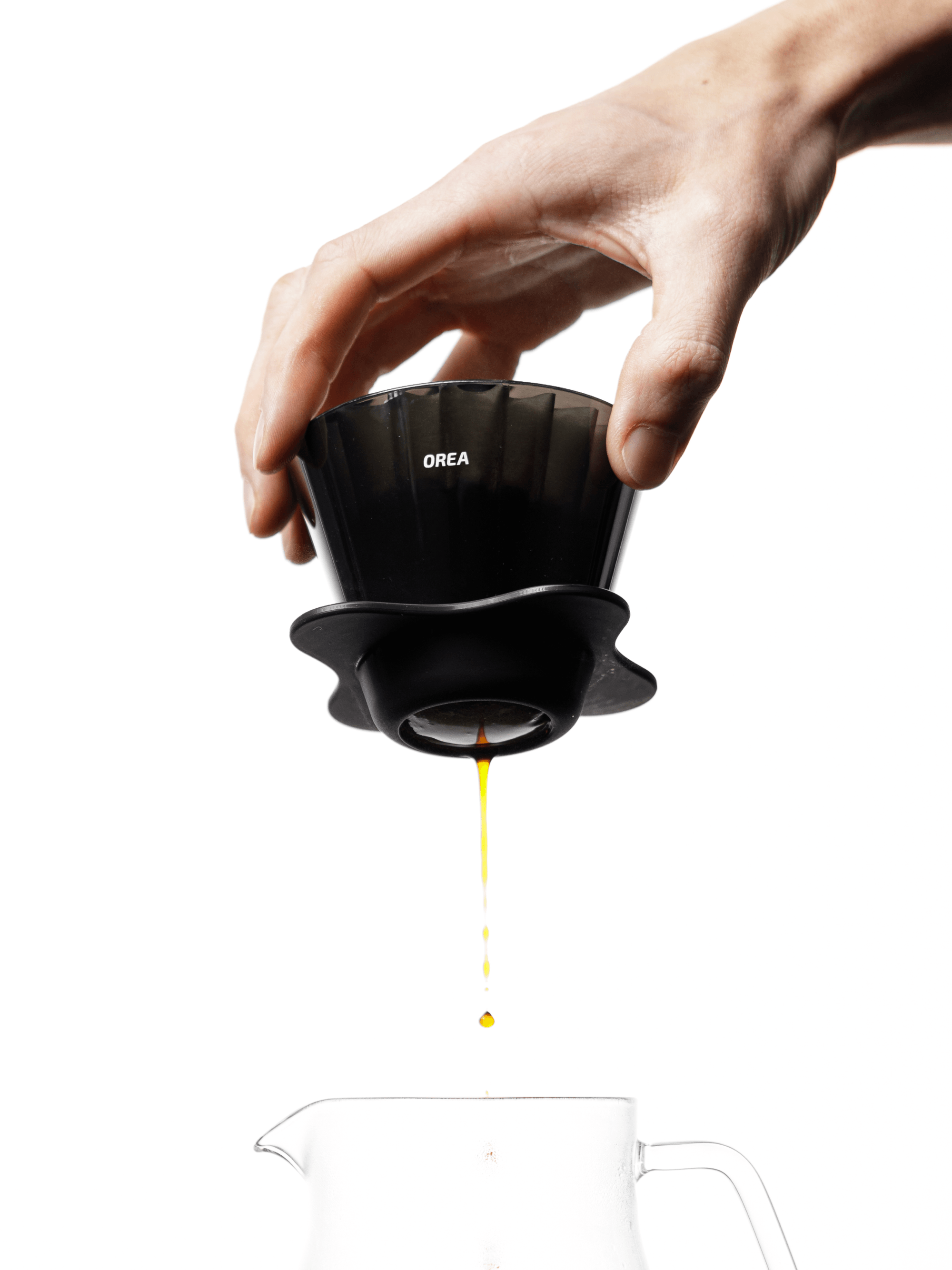 A hand lifting the OREA O2 Brewer over a clear glass carafe as a clean, amber stream of freshly brewed coffee falls perfectly through the open bottom, highlighting its flawless flow dynamics.