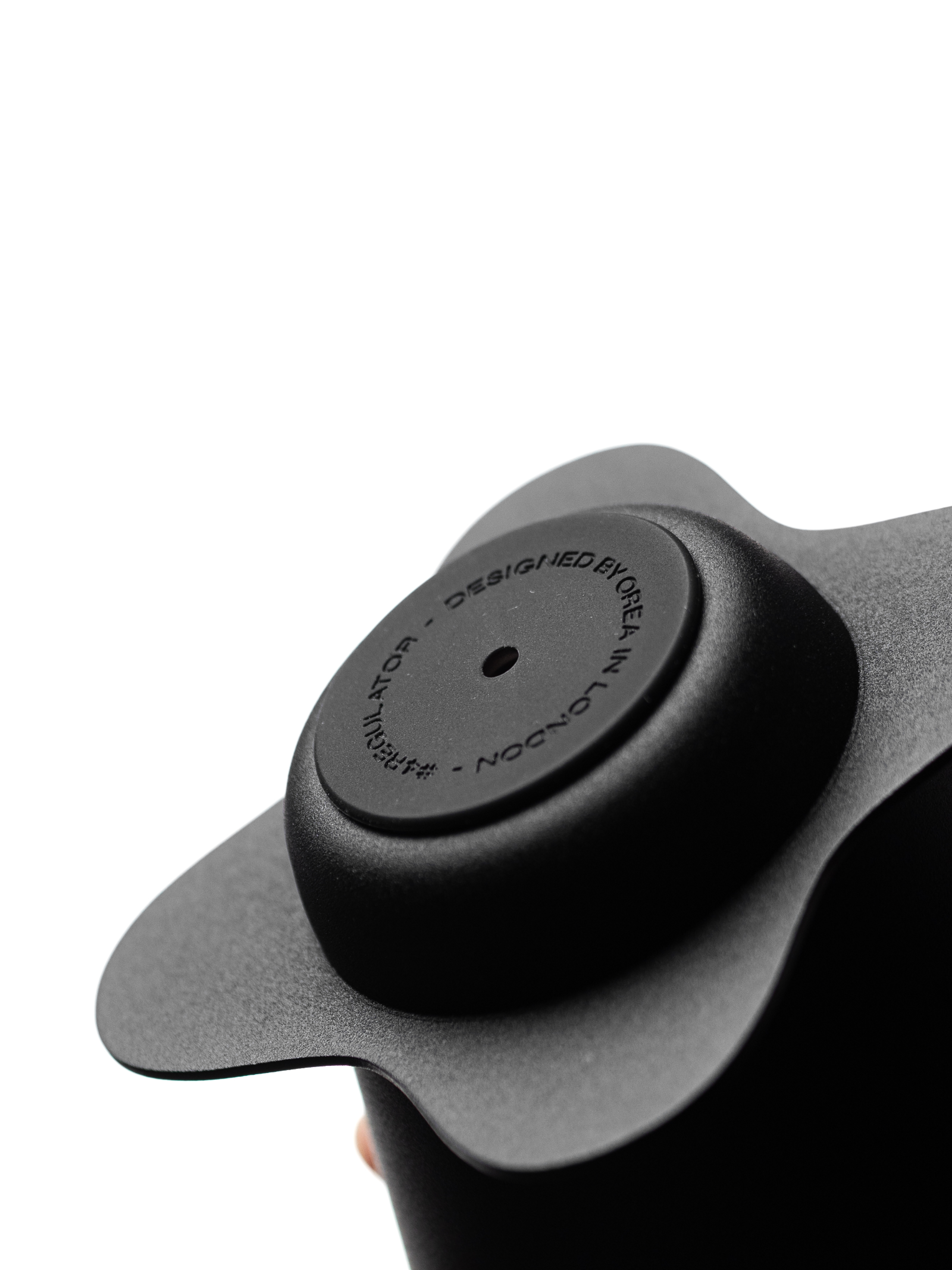 An extreme close-up of the matte black, textured base plate of the OREA O2 brewer, featuring the minimalist, laser-engraved circular text reading "DESIGNED BY OREA IN LONDON", showcasing premium build quality.