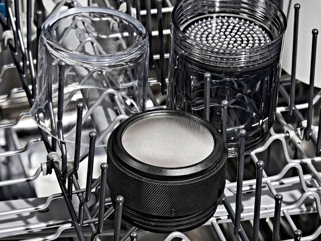 Clear and black components of the OXO Brew Rapid Brewer sitting neatly in a dishwasher rack, highlighting the easy cleaning and dishwasher-safe design of the stainless steel filter and Tritan carafe.