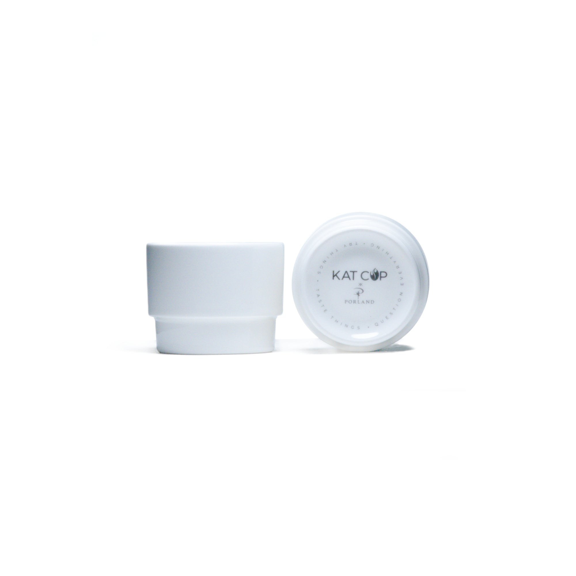 A clean, bright studio product shot of a white Porland KAT CUP in two views—one upright showing its minimalist cylindrical shape, and one inverted displaying the distinctive KAT CUP logo and stamp on the base.