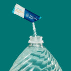 A single mineral stick being emptied into the top of a clear plastic gallon water bottle against a solid teal background.